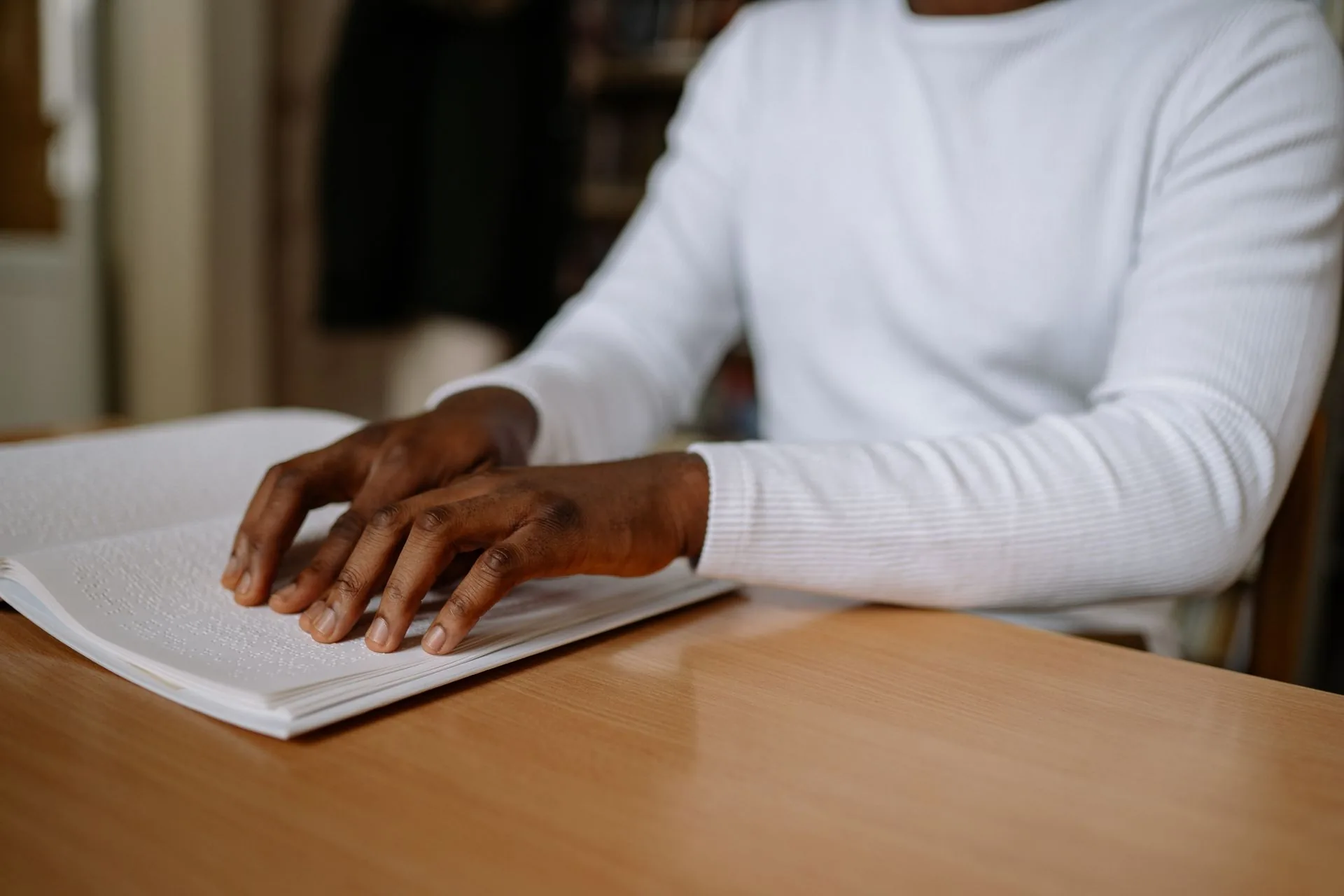 A person's hands reading a braille book at a table