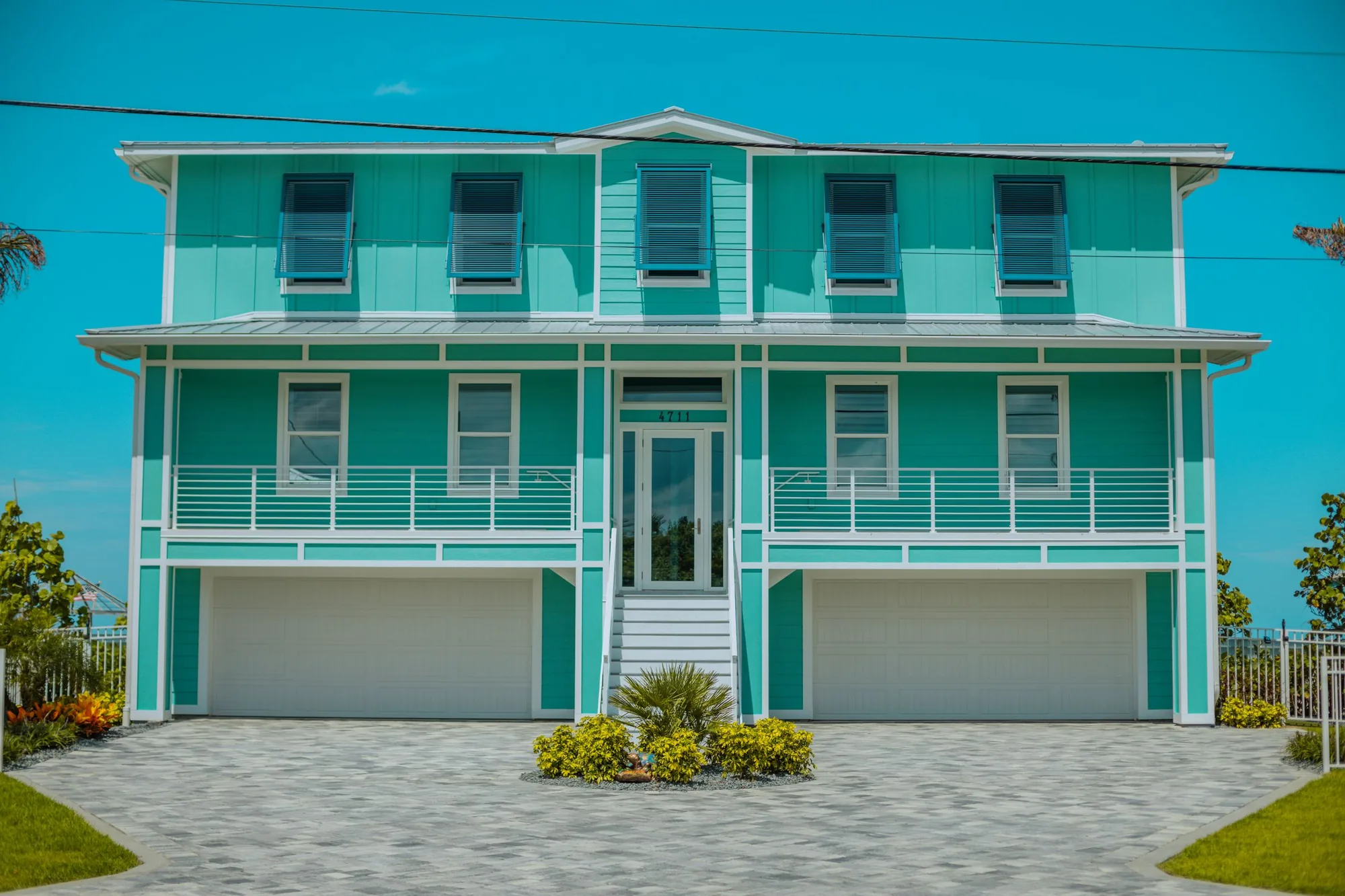 A teal two-story coastal Florida home with covered balconies and a paver driveway