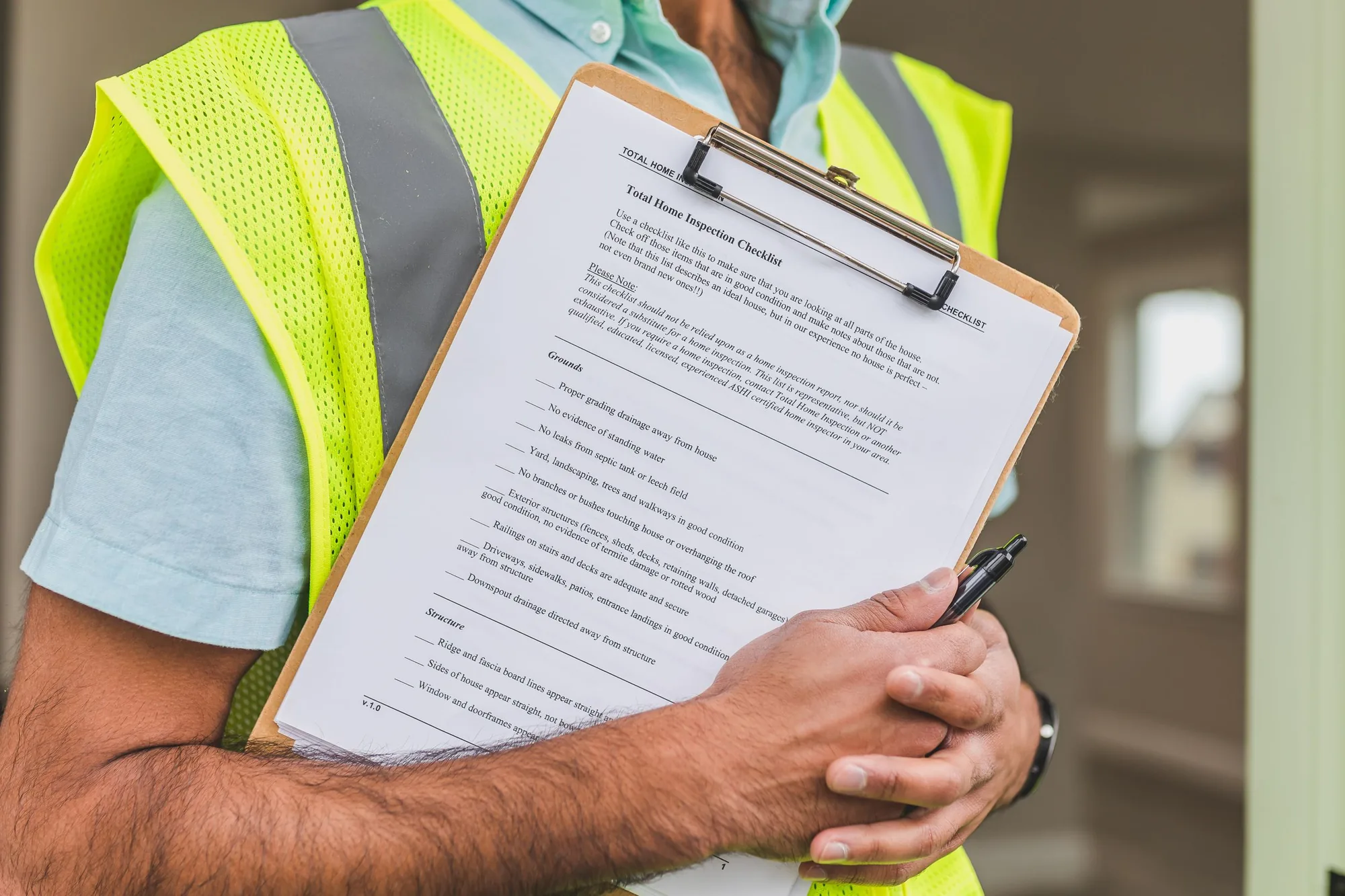 An inspector in a safety vest reviewing a total home inspection checklist on a clipboard