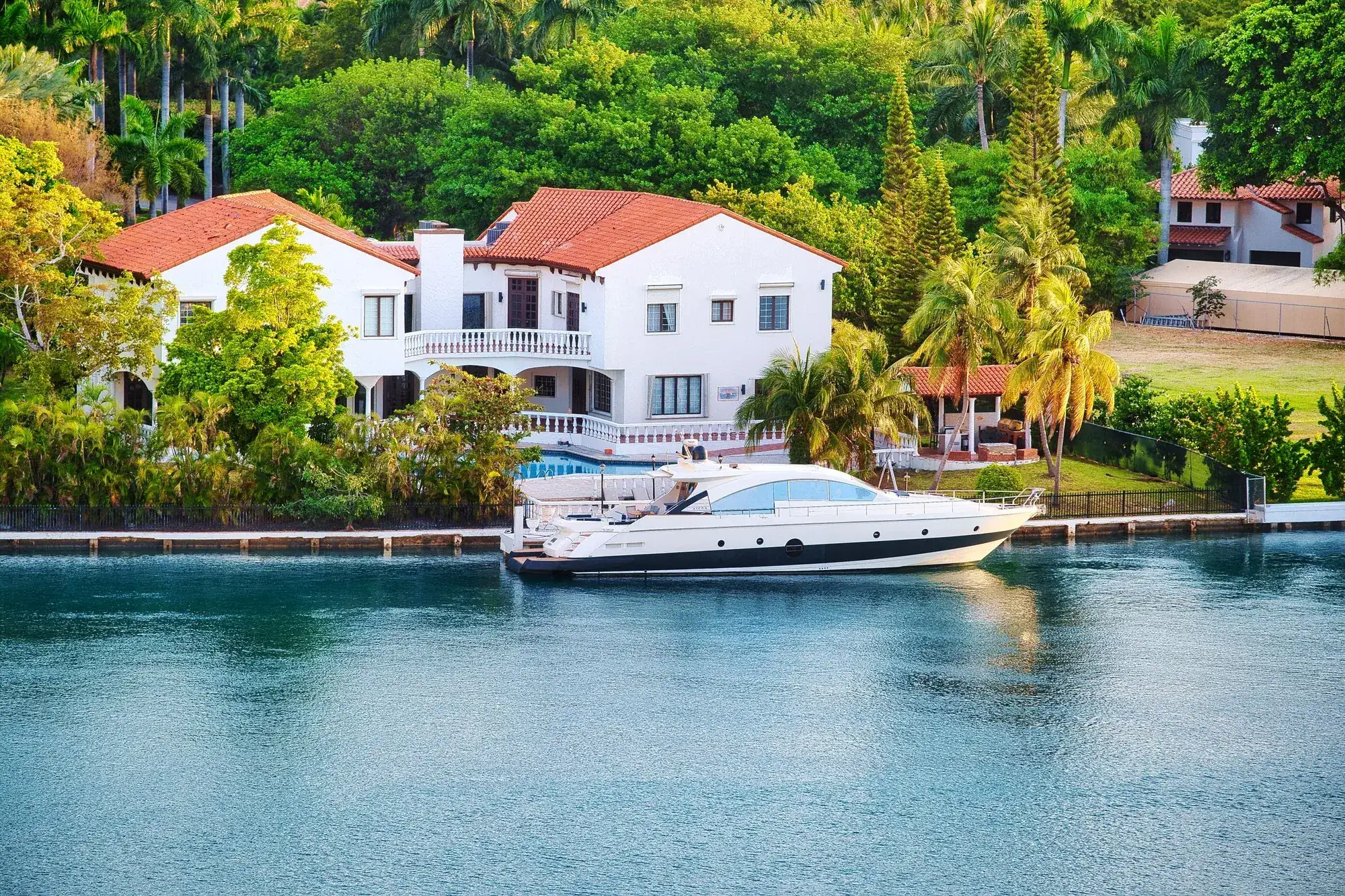 A white Mediterranean-style waterfront home with a tile roof and a docked boat on a Florida canal