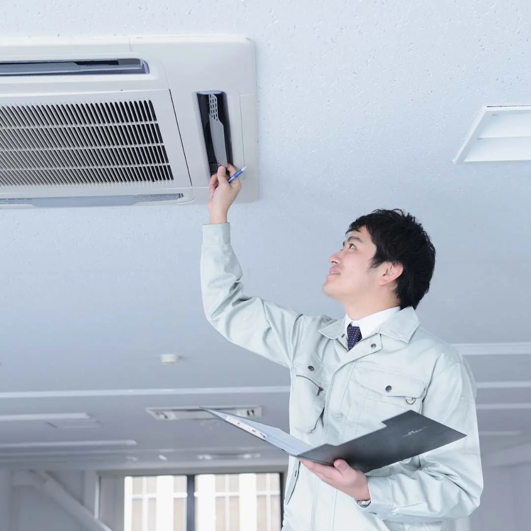A technician inspecting an HVAC ceiling unit and taking notes on a clipboard
