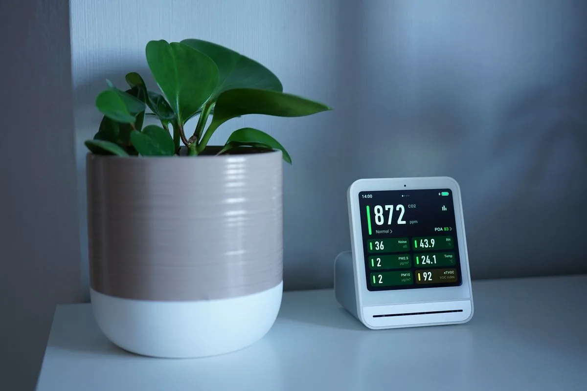 An indoor air quality monitor on a table next to a houseplant, displaying CO2 and humidity readings