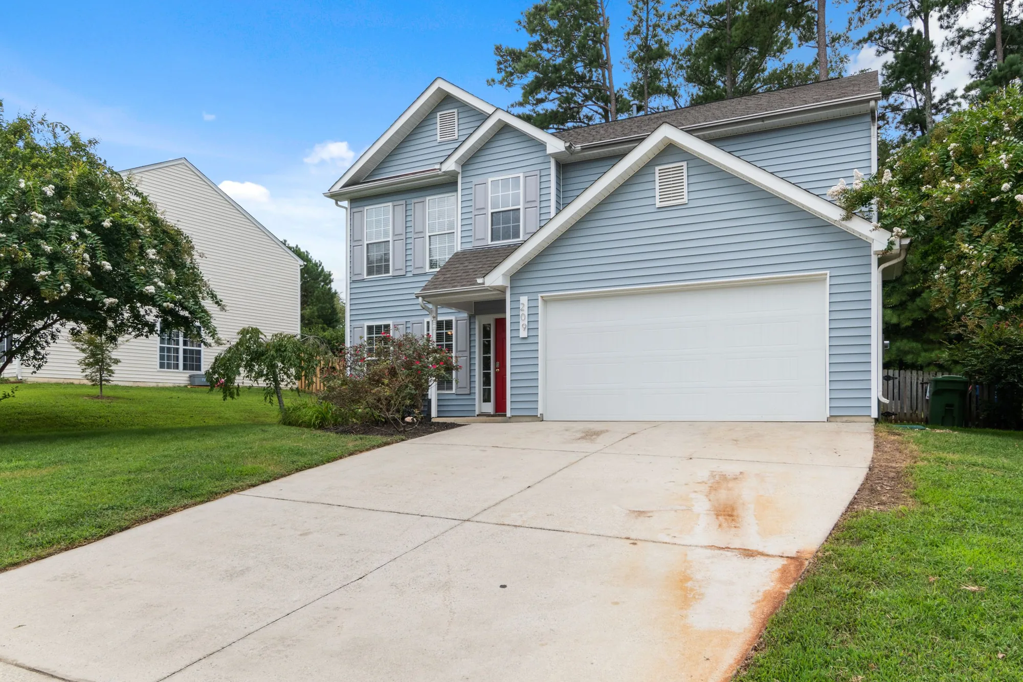 A blue-gray two-story Florida home with a red front door and a landscaped front yard
