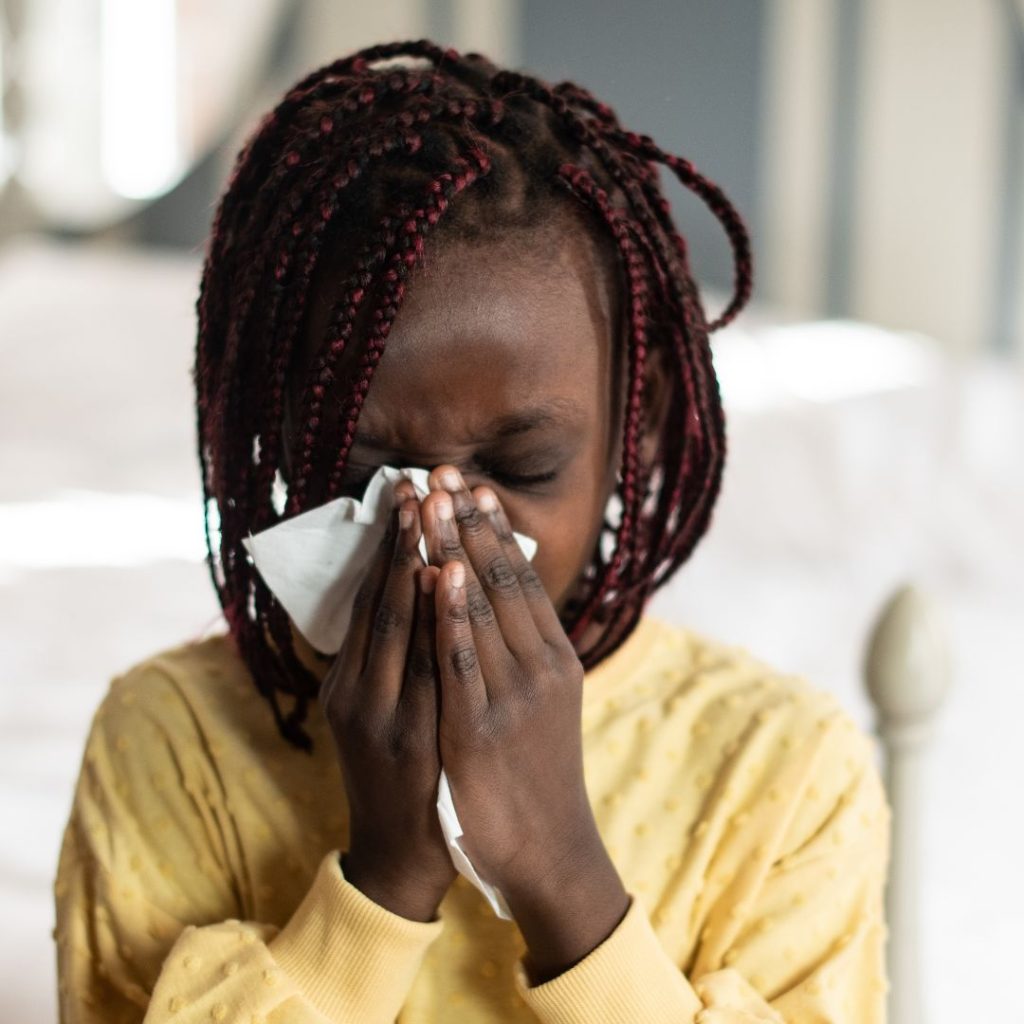 An image of a child experiencing toxic mold symptoms jacksonville. She's shown blowing her nose into a Kleenex